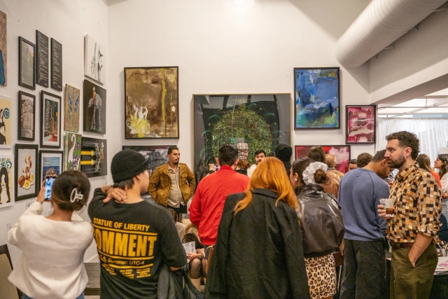 A packed opening night in the Emerging Gallery, work hung floor to ceiling around a large peacock painting.