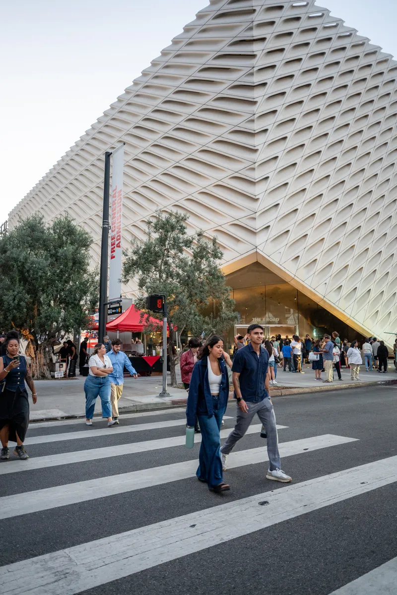 Pedestrians crossing Grand Avenue beneath The Broad’s honeycomb facade.